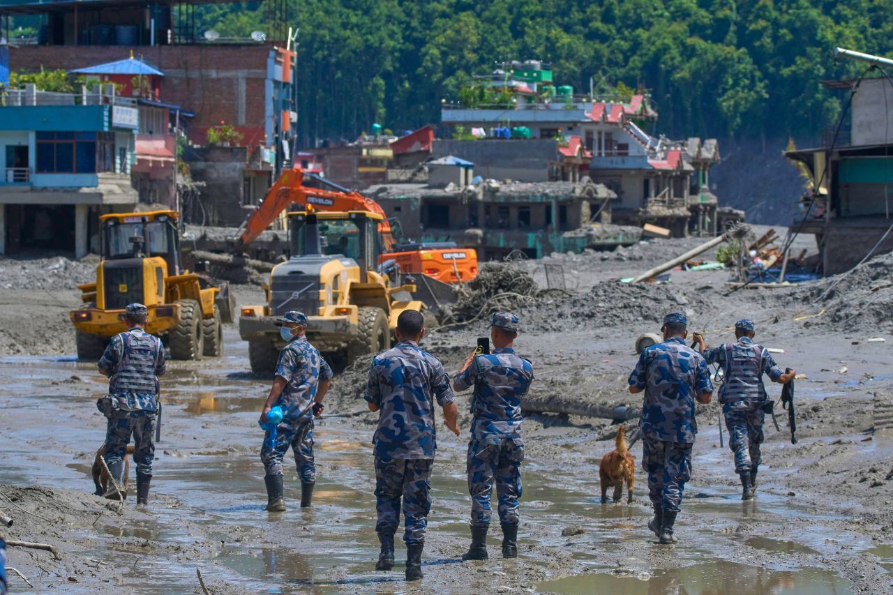 Nepalese policemen watch as earthmovers clear the debris of flash flooding in Nepal's Nuwakot district, Thursday, Aug. 27.