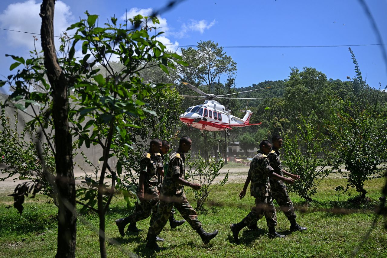 Army personnel walk past a helicopter landing with rescued flood-affected residents at an army camp in Nepal's Nuwakot district on August 27.